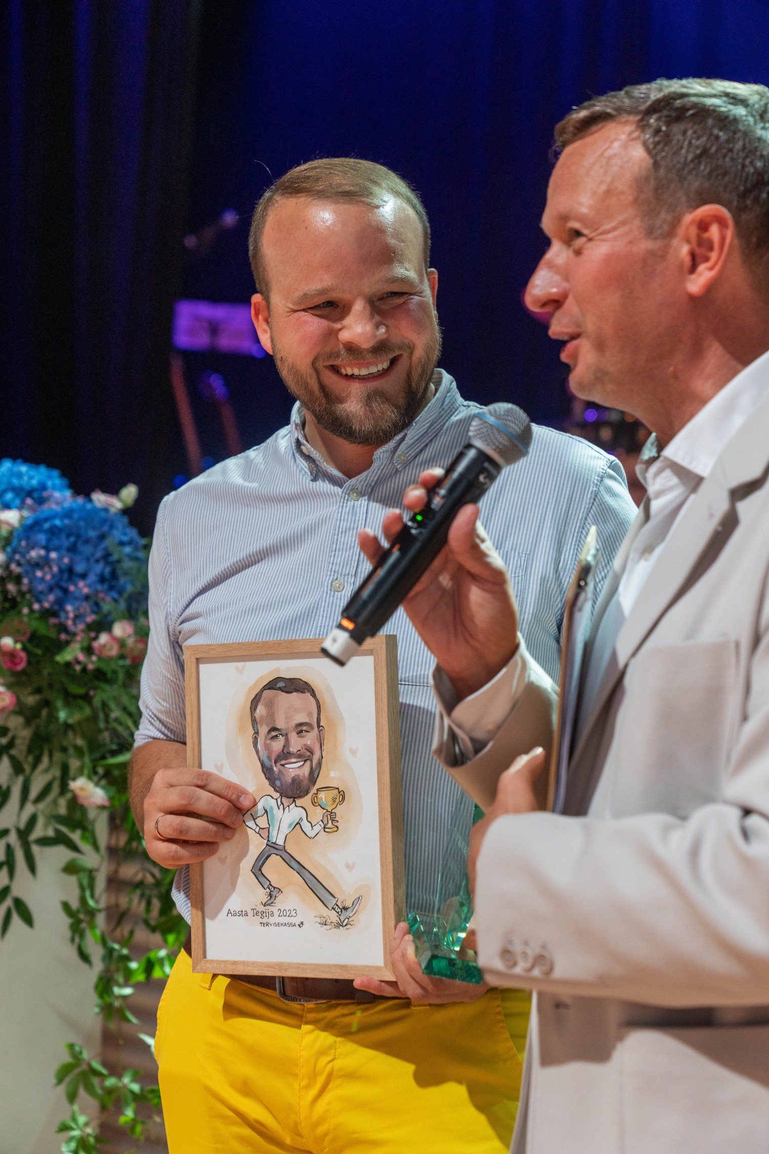 Marko Tähnas on Tervisekassa 2023. aasta tegija. Foto: erakogu Kaks meesterahvast seisavad, vasakul oleval käes pildiraam ja paremal käes mikrofon